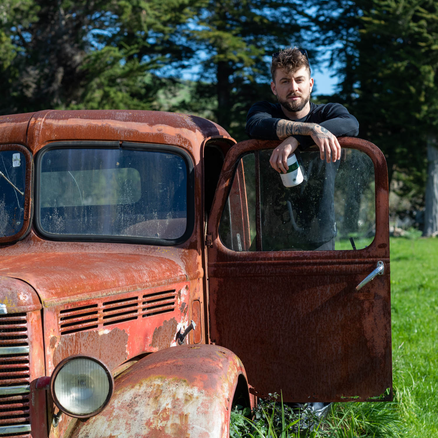 Emile Siers-Jamieson, founder of REGEN+, holding a container of organic supplements, standing by a farm vehicle